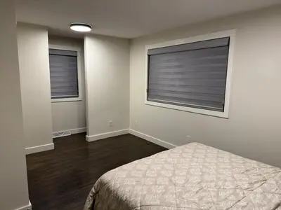 a bedroom with a bed and two windows with blinds at Luxurious Air Conditioned Inner City Bungalow in Calgary
