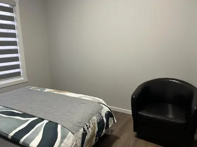 a bedroom with a bed and a black chair at 1-bedroom private suite, 20 minutes from the airport, with a kitchen in Edmonton
