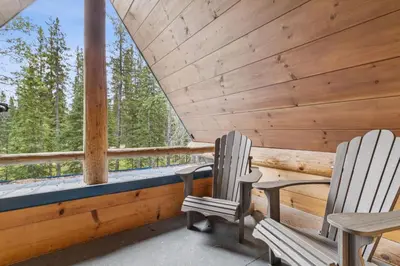 two chairs sitting on the porch of a cabin with trees at Nordegg Timber Estate in Nordegg