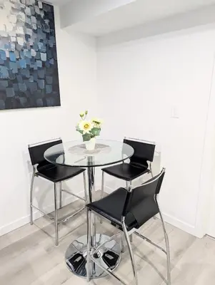 a glass table with black chairs and a vase of flowers at Basement Suite in Desrochers SW in Edmonton