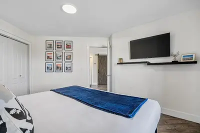 a white bedroom with a bed and a flat screen tv at Lakefront Lookout 1BR Condo on Lakeshore Drive in Sylvan Lake