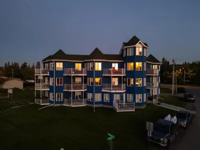 a large blue house with a car parked in front of it at Lakefront Lookout 1BR Condo on Lakeshore Drive in Sylvan Lake