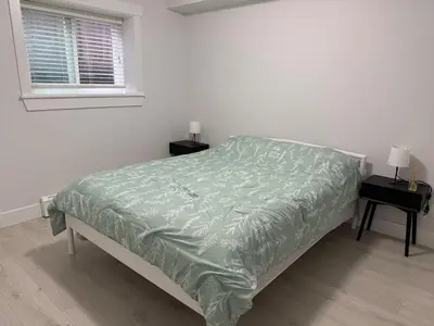 a bedroom with a bed with a green comforter and a window at Private two bedroom basement suite Sleeps six people in Surrey