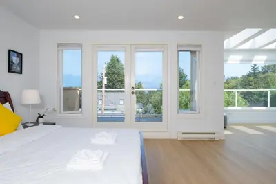 a white bedroom with a bed and windows at Elegant Spanish Villa with Ocean & Mountain Views in Vancouver