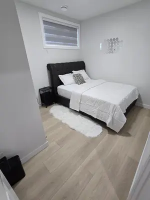 a bedroom with a bed with white sheets and a wooden floor at Cozy Modern Spacious 2 Bedroom and full kitchen in Southwest Calgary in Calgary