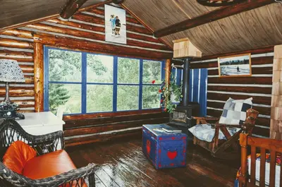 a living room with wooden walls and windows in a cabin at Country Rustic Loghouse at Teepee Meadows in Valemount