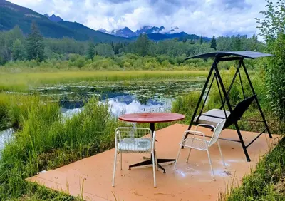 a table and two chairs sitting next to a lake at Country Rustic Loghouse at Teepee Meadows in Valemount