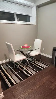 a glass table and two white chairs on a rug at Oasis at Heritage in Fort McMurray