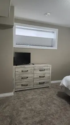 a bedroom with a dresser with a television and a window at Oasis at Heritage in Fort McMurray