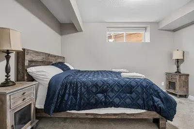 a bedroom with a bed with a blue blanket and a window at Cozy & Large Furnished 2-Bedroom Suite in Calgary