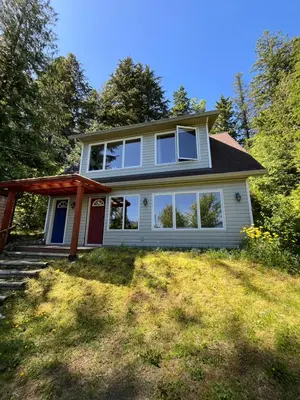 a white house with a red door and trees at Lake View Suite, Forest Retreat, Balfour BC in Balfour