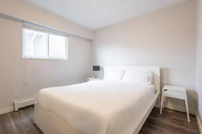 a white bedroom with a large bed and a window at Sleek Modern Escape Suite - Comfort and Style in the City in Vancouver
