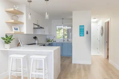 a white kitchen with blue cabinets and white counters at High Tide Suite - New Bright Oceanfront Escape with Spa-like Bath in Nanoose Bay
