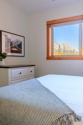 a white bedroom with a bed and a window at Bluebird - Spacious Luxury Shared Rooftop Hot Tub in Canmore