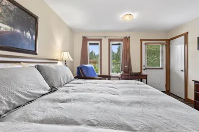 a bedroom with a bed and a chair and windows at Ackerview Guesthouse Bed and Breakfast in Salmon Arm