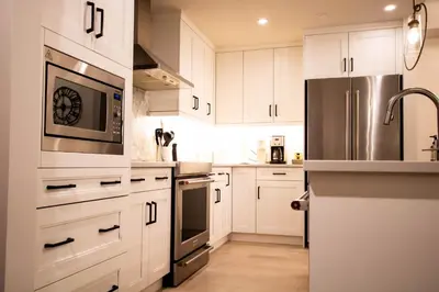 a kitchen with white cabinets and a stainless steel refrigerator at Luxury Spring Creek Condo with Hot Tub in Canmore