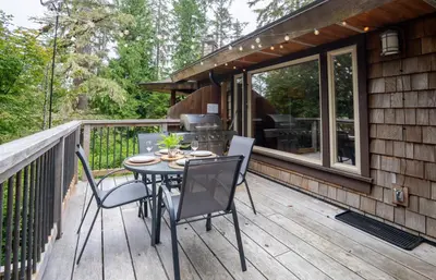 a patio with a table and chairs on a deck at South Swell Tofino (formerly Blue Heron Waterfront Home amid Old Growth Cedars) in Tofino