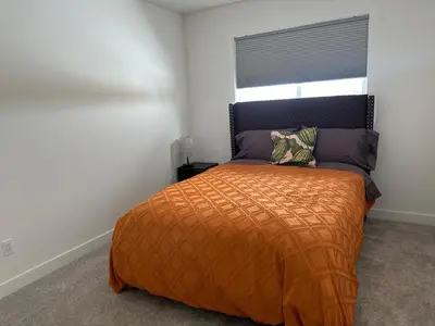 a bedroom with a bed with an orange comforter and a window at Modern new townhouse in Red Deer