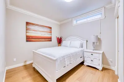 a white bedroom with a bed and a painting on the wall at Cozy two beds lower level suite in Vancouver West in Vancouver