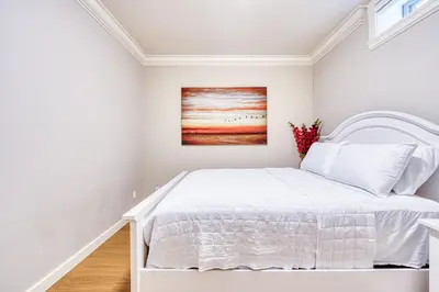 a white bedroom with a bed and a painting at Cozy two beds lower level suite in Vancouver West in Vancouver