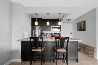 a kitchen with black cabinets and two bar stools at Central Downtown at Rocky Mountain Court with Gym, Court, Sauna and Secured Parking in Calgary