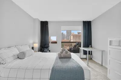 a white bedroom with a large bed with a teddy bear on it at Central Downtown at Rocky Mountain Court with Gym, Court, Sauna and Secured Parking in Calgary