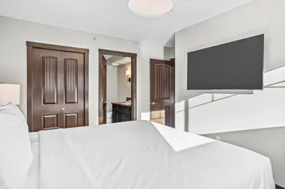 a bedroom with a white bed and a flat screen tv at Bears Den 2BR Getaway with Hot Tub, BBQ Near DT in Dead Man's Flats