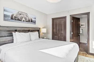 a bedroom with a white bed and a picture of a bear at Bears Den 2BR Getaway with Hot Tub, BBQ Near DT in Dead Man's Flats