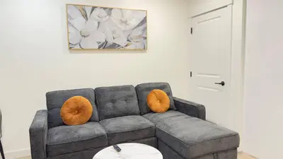 a living room with a gray couch with orange pillows at Northern Nook - 2BR Suite in Calgary