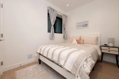 a white bedroom with a bed and a window at Brand New Cozy Suite near Collingwood School in West Vancouver