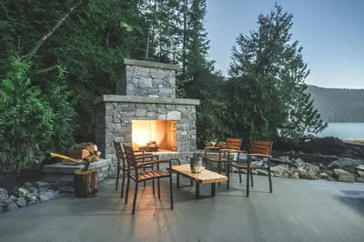a patio with a stone fireplace and chairs and a table at Wild Renfrew Seaside Cottages in Port Renfrew