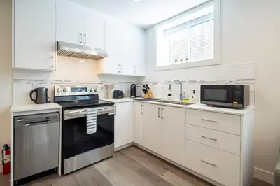 a kitchen with white cabinets and a black stove top oven at Relaxing 2BR Stay - Kitchen & Central Convenience in Vancouver