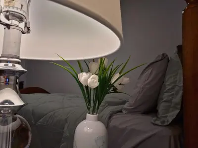 a white vase with flowers in it next to a bed at Sunny's Homes in Edmonton