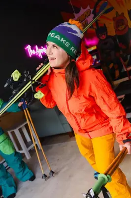 a young woman is holding skis on a tripod at The Après Arcade in Sun Peaks
