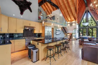 a large kitchen with bar stools and a living room at Luxury Whistler 6BR Chalet, Hot Tub and Music Loft in Whistler