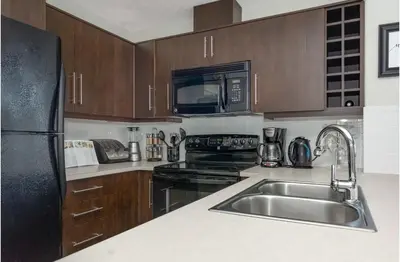 a kitchen with a sink and a black refrigerator at The Spruce Modern 2BR Condo with Pool & Parking in Calgary