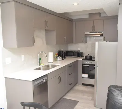 a kitchen with white cabinets and a sink and a refrigerator at Beautiful Basement Suite in Stillwater, West Edmonton in Edmonton