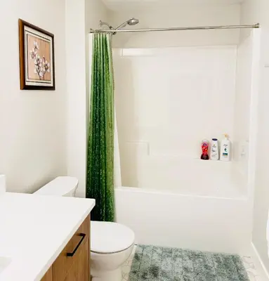 a bathroom with a toilet and a green shower curtain at Casa Del Mar-A family Suite in Victoria in Langford