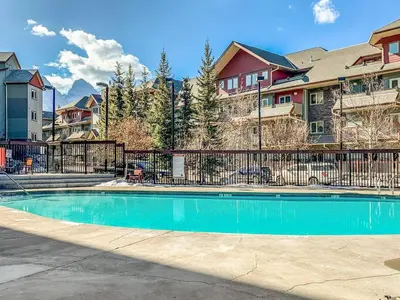 a swimming pool in front of a fence with houses at Lovely 2BR Canmore Condo w Heated Pool and Hot Tub in Canmore