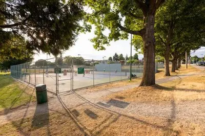 a fence with a tree and a tennis court at 2BR Suite Close to Transit - Great for FIFA Vancouver in Burnaby