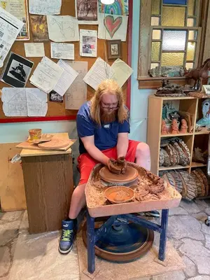 a woman sitting on a table making a pottery wheel at Cozy Country Log Cabin Art Spa Getaway in Caroline