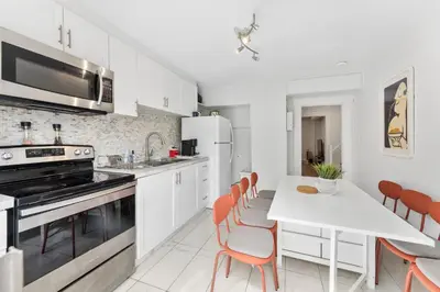a kitchen with white cabinets and a white table with orange chairs at Heritage Home in Heart of City with free Parking in Vancouver