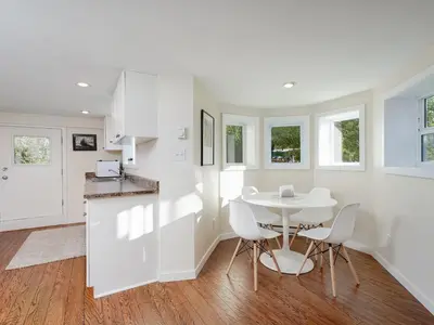 a kitchen and dining room with a white table and chairs at Gallery Garden - stylish, art-filled 1-bedroom suite by Victoria Prime! in Victoria