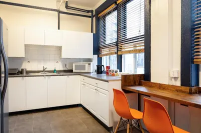 a kitchen with white cabinets and orange chairs at The Guesthouse Vancouver Downtown in Vancouver
