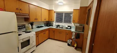 a kitchen with wooden cabinets and a white refrigerator at Spacious Family Room with Shared Washroom in Vancouver