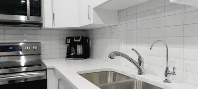 a white kitchen with a sink and a microwave at Cozy Luxe Suites in Calgary