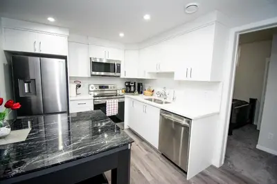 a kitchen with white cabinets and stainless steel appliances at Cozy Luxe Suites in Calgary