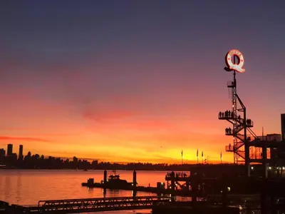 a sunset over a body of water with a clock at Spacious 1BR Suite Near Capilano Bridge & Trails in North Vancouver