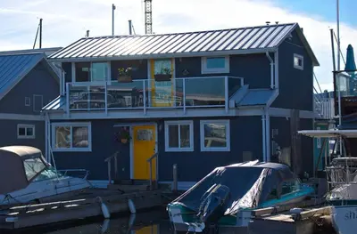 a blue house with a yellow door next to a boat at Cozy modern floating home next to Lonsdale Quay in North Vancouver
