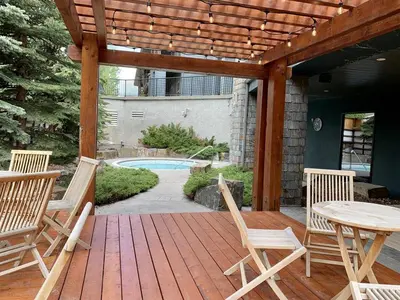 a wooden deck with chairs and a table and a pool at Stunning Condo - Hot Tubs & Steam Room - Pets Ok in Canmore